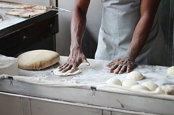 A baker in an indoor kitchen kneading dough for bread preparation, showcasing traditional baking techniques. HD wallpaper