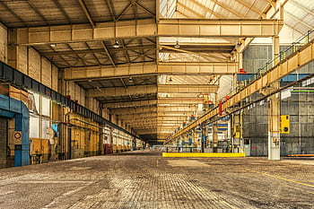 Expansive interior of an industrial warehouse showing steel beams, high ceilings, and ample space. HD wallpaper
