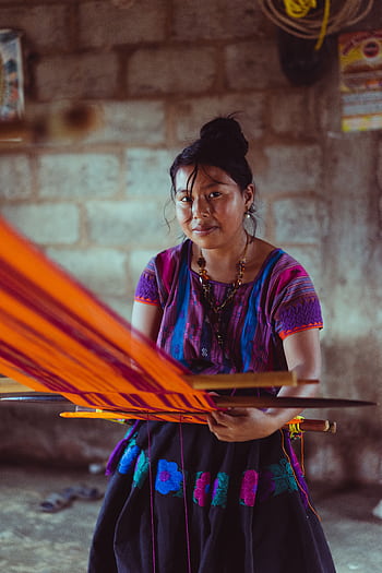 Indigenous Mexican woman weaving colorful fabric on a traditional loom inside a rustic setting. HD phone wallpaper