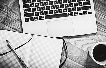 Black and white of a workspace featuring a laptop, notebook, pen, and coffee cup. HD wallpaper