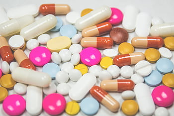 A mix of colorful pills and capsules scattered on a white surface, representing pharmaceuticals. HD wallpaper