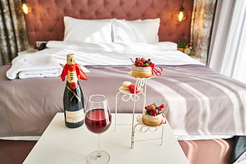 Elegant bedroom setting with champagne, wine glass, and desserts, creating a cozy ambiance. HD wallpaper