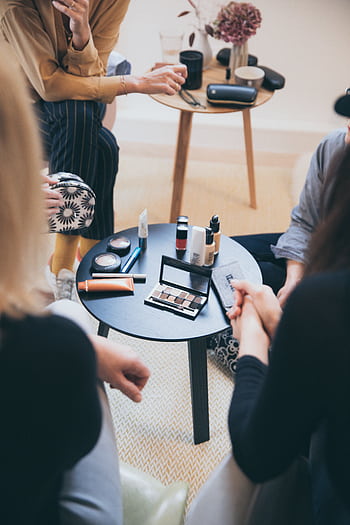 Women gathered around a table applying cosmetics, fostering a collaborative workspace. HD phone wallpaper