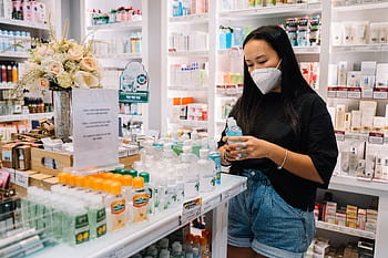 Asian woman selecting hand sanitizer in a well-stocked pharmacy, emphasizing health and hygiene. HD wallpaper