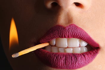 Bold close-up of lips with vivid lipstick holding a lit matchstick, creating a fierce and dynamic . HD wallpaper