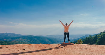 A man raises his arms in triumph on a rocky mountain summit overlooking a vast landscape HD wallpaper