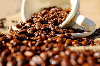 Close-up of coffee beans spilling from a cup onto a burlap surface, perfect for coffee lovers. HD wallpaper