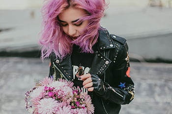 A stylish young woman with purple hair holding a bouquet, wearing a black leather jacket outdoors. HD wallpaper