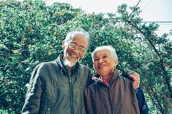 Senior couple enjoying a joyful moment together in a lush garden setting, exuding love and happiness. HD wallpaper