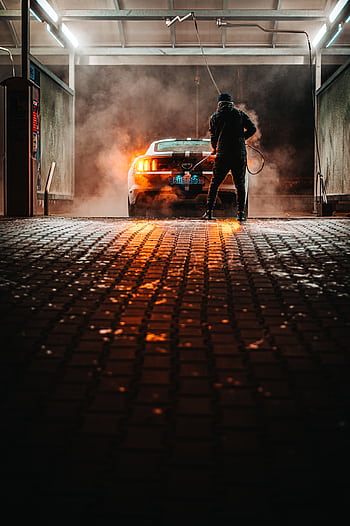 A person washing a sports car at a carwash during the night, illuminated by lights. HD phone wallpaper