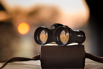 Close-up view of binoculars on a surface with sunset reflection in lenses. HD wallpaper
