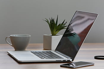 Minimalist home office desk with laptop, smart, and plant for a modern work environment. HD wallpaper