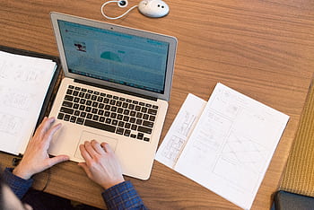 An overhead view of a person working on a laptop at a desk with documents and papers. HD wallpaper