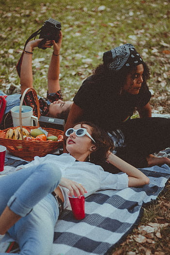 A relaxed picnic scene with friends enjoying a lazy afternoon outdoors on a grassy field. HD phone wallpaper