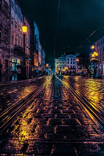 Moody cobblestone street in Lviv, Ukraine, illuminated at night with vibrant city lights and wet reflections. HD phone wallpaper