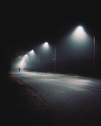 Silhouette of a person walking under streetlights on a foggy night in Coesfeld, Germany. HD phone wallpaper