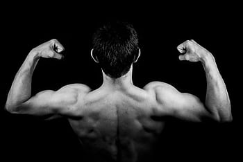 Black and white of a muscular man flexing arms against a dark background. HD wallpaper