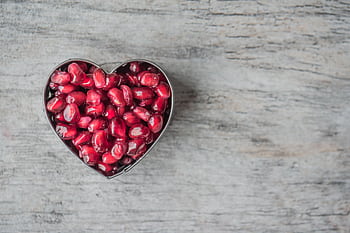 Delicious and juicy pomegranate seeds in a heart-shaped bowl on a wooden table. HD wallpaper
