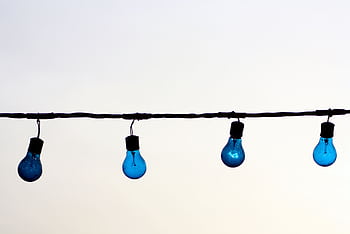 Minimalist of blue light bulbs hanging on a wire against a neutral sky background, offering creative copyspace. HD wallpaper