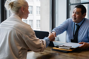 Two professionals in an office setting shaking hands after a business agreement. HD wallpaper