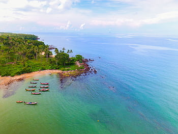 Aerial view of a serene tropical beach with docked boats and lush greenery along the coastline. HD wallpaper