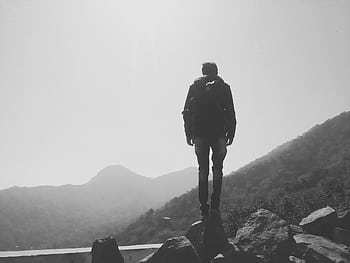 A lone hiker stands on rocks, overlooking misty mountain landscape, capturing the essence of adventure. HD wallpaper