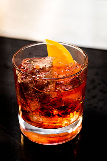 Chilled cocktail with orange slice garnish in a glass on a dark surface. HD phone wallpaper