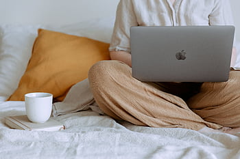 A woman casually working on a laptop with a coffee cup in a cozy bedroom setting. HD wallpaper