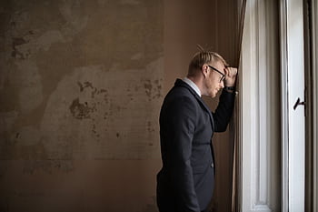 A worried businessman in a suit leaning against a window, expressing stress and concern. HD wallpaper