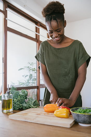 Smiling woman in kitchen slicing bell peppers, promoting healthy eating and joy in food preparation. HD phone wallpaper