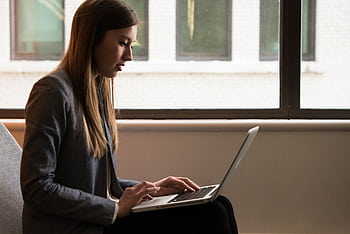 Professional woman using laptop in modern indoor setting. Ideal for business or technology themes. HD wallpaper
