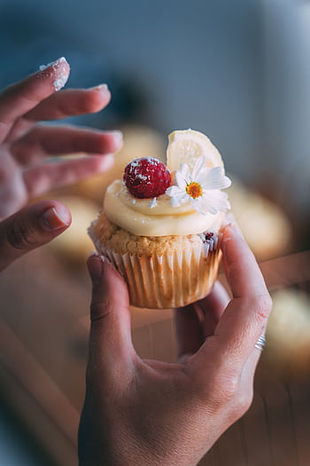 Close-up of a cupcake topped with raspberry, cream, and edible flower held by hands. HD phone wallpaper