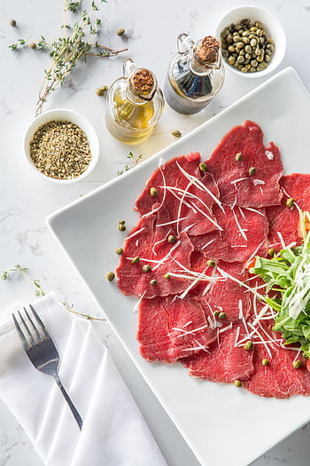 Delicious beef carpaccio with capers, olive oil, and fresh toppings on a white plate. HD phone wallpaper