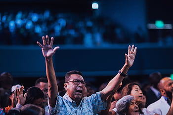 Diverse group of people engaging in worship with hands raised indoors. HD wallpaper