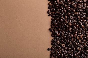 A close-up overhead shot of roasted coffee beans scattered on a brown surface, offering copy space. HD wallpaper
