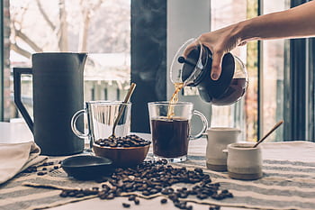 Inviting scene of fresh coffee being poured with scattered coffee beans on a wooden table. HD wallpaper