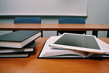 Books and a tablet on a desk in a classroom, depicting modern education. HD wallpaper