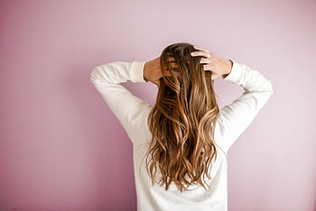 Back view of a woman with elegant long brown hair against a pink wall, showcasing stylish hair design. HD wallpaper