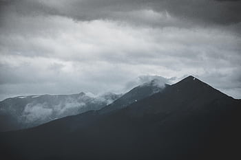 A moody mountain landscape shrouded in clouds and mist creating a dramatic atmosphere. HD wallpaper