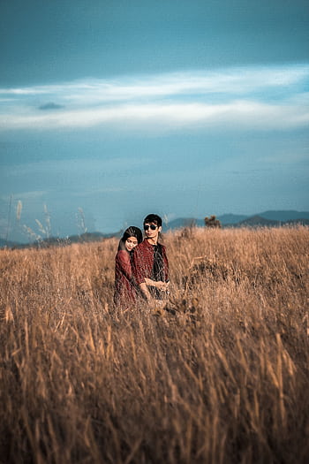 A young couple embraces in a peaceful hayfield, surrounded by golden grass under a bright blue sky. HD phone wallpaper