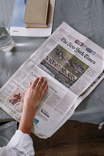 Person reading The New York Times at home with books and glass of water on the table. HD phone wallpaper