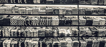 Black and white showcasing neatly folded t-shirts stacked on store shelves. HD wallpaper