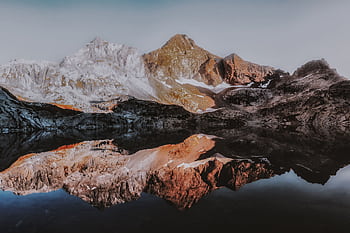 Stunning mountain landscape with snow-capped peaks reflecting in a calm lake, showcasing nature's serenity. HD wallpaper