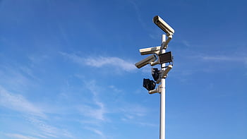 Multiple security cameras on a pole with a clear blue sky backdrop. HD wallpaper