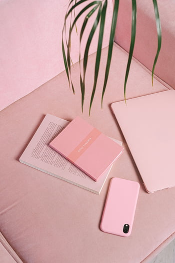 Modern flat lay of pink gadgets, books, and greenery on a pink sofa, creating a trendy workspace. HD phone wallpaper