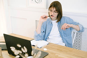 Woman working thoughtfully in home office, reflecting on ideas with laptop and notebook. HD wallpaper