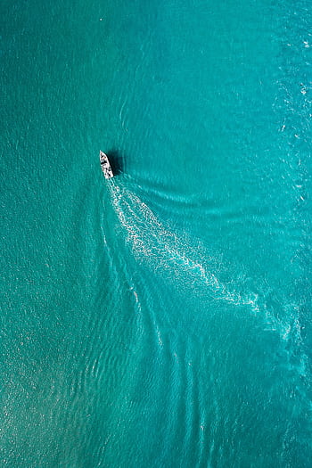 A serene aerial view of a boat navigating through vibrant turquoise waters, leaving a trail. HD phone wallpaper