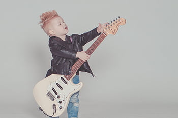 Stylish young boy with a mohawk strumming an electric guitar, wearing a leather jacket and blue jeans. HD wallpaper