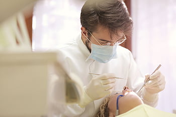 Dentist in face mask conducting a dental examination with tools in clinic setting. HD wallpaper