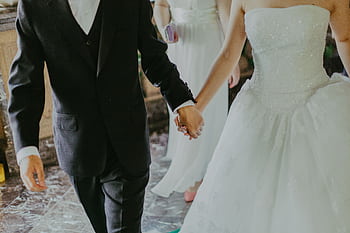A romantic moment capturing a bride and groom holding hands in elegant wedding attire indoors. HD wallpaper